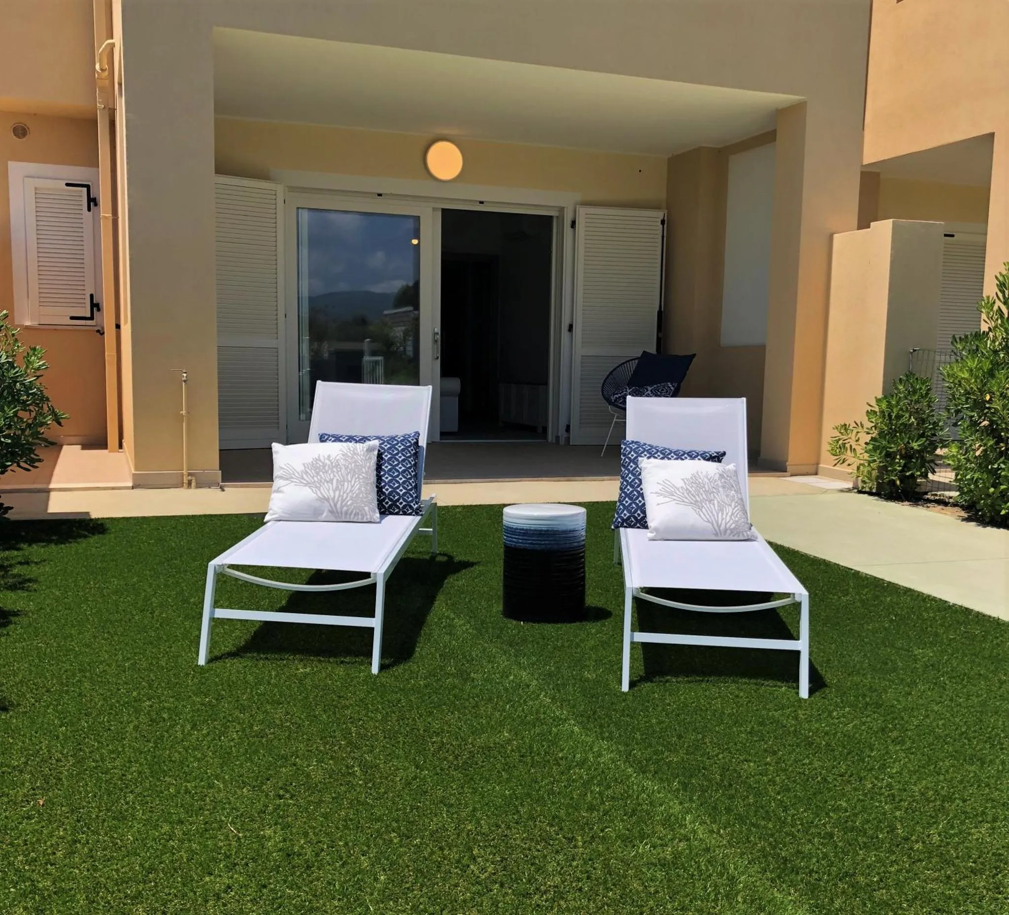 Deux transats bleus et blancs sur une pelouse artificielle devant une terrasse.