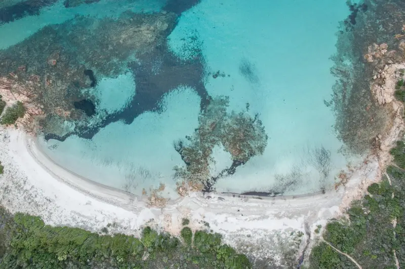 Vue aérienne d'une crique aux eaux turquoise et au sable blanc.