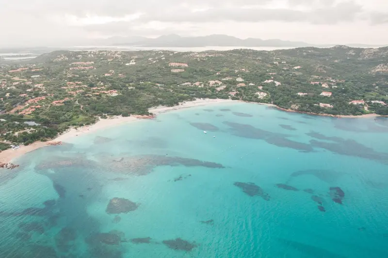 Vue aérienne d'une plage de sable blanc bordée d'une eau turquoise et d'une végétation luxuriante.
