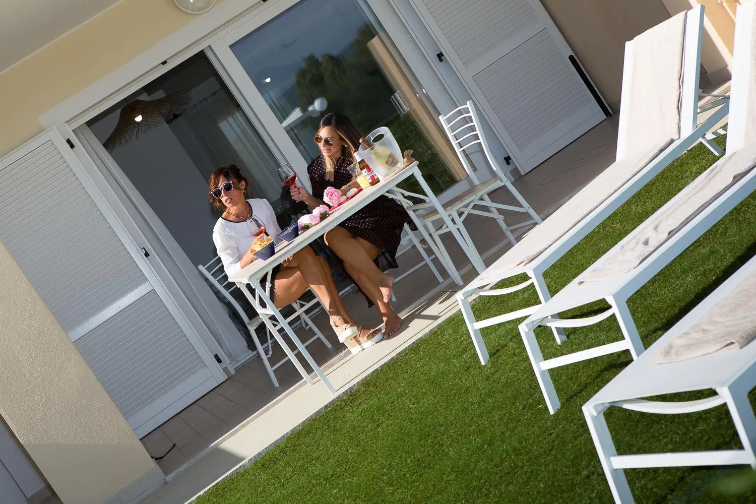 Deux femmes sont assises à une table sur une terrasse ensoleillée.