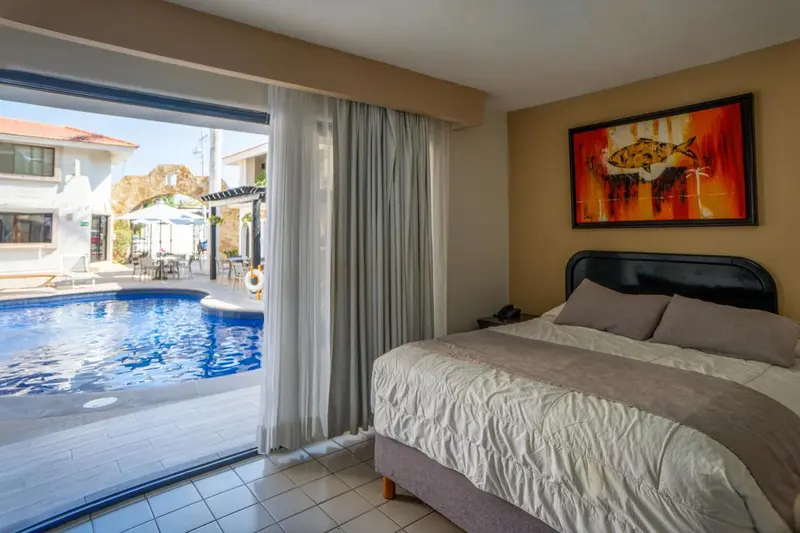 Chambre lumineuse avec un lit et vue sur une piscine.