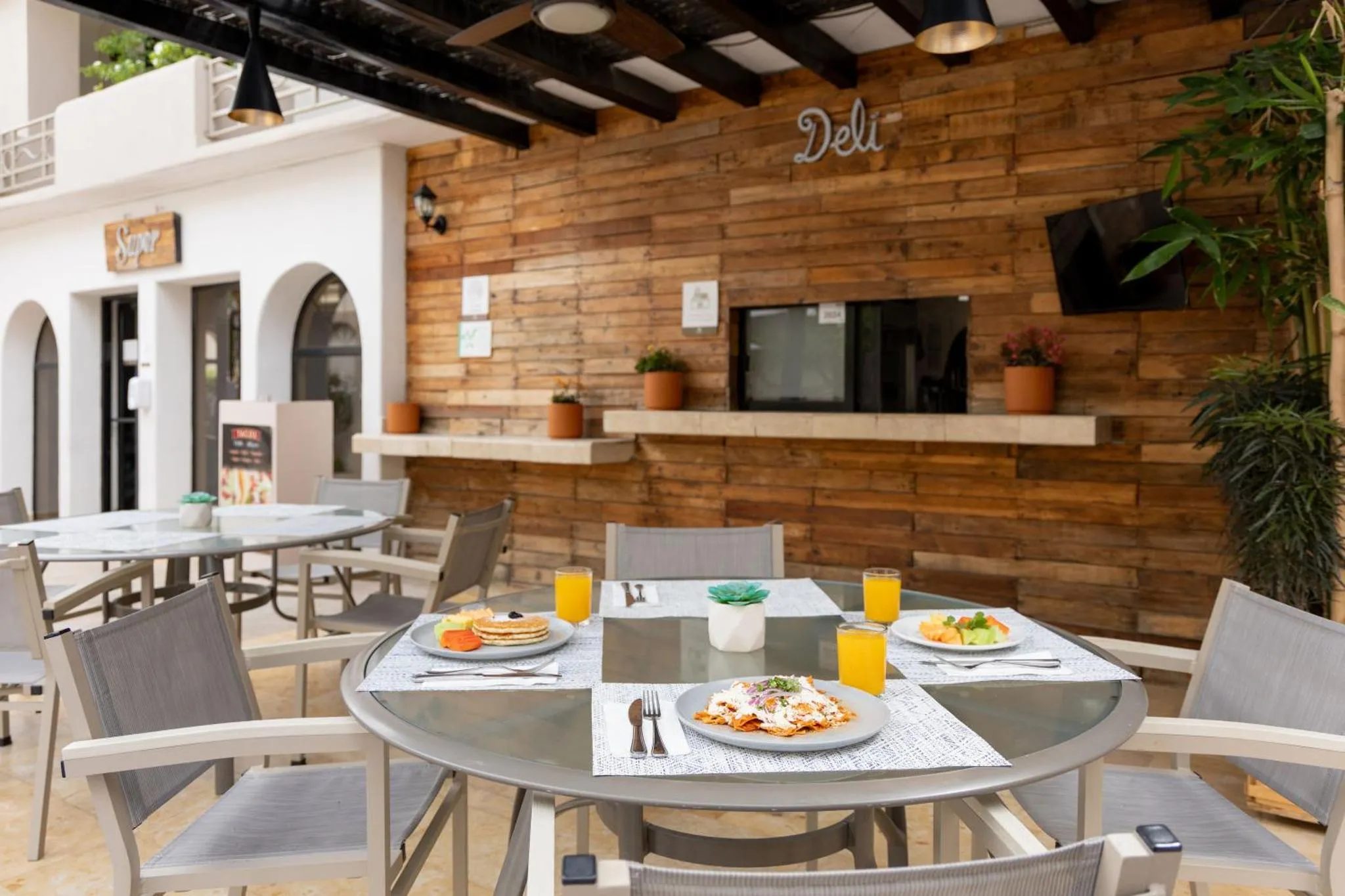 Une table est dressée avec des plats et des boissons sur une terrasse ombragée.