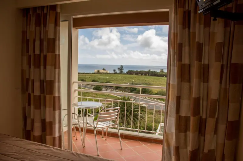 Une terrasse avec une table et des chaises offre une vue sur la mer et la végétation.
