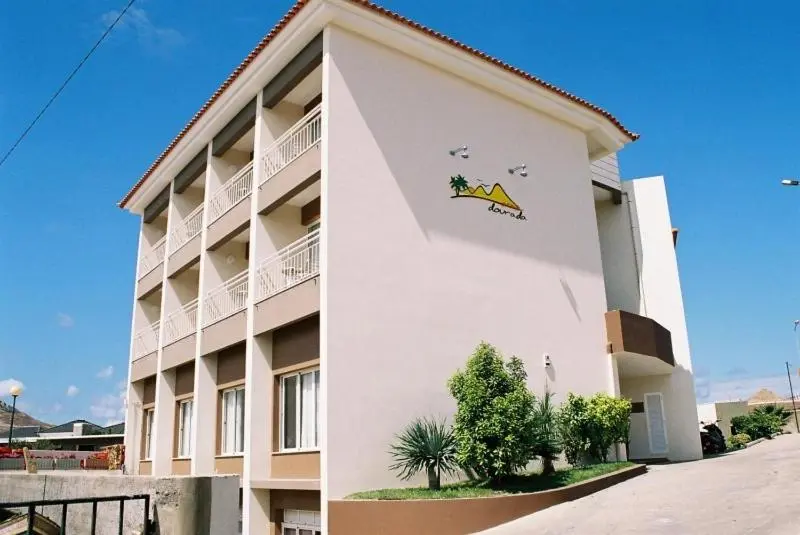 Façade d'un bâtiment beige à deux étages avec des balcons et une végétation devant.