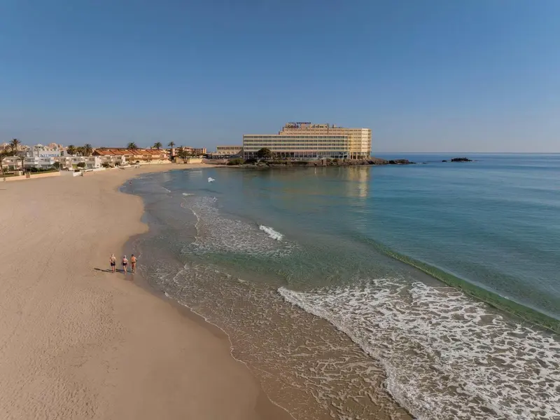 Vue aérienne d'une plage de sable fin bordée d'eaux turquoise et d'un hôtel.
