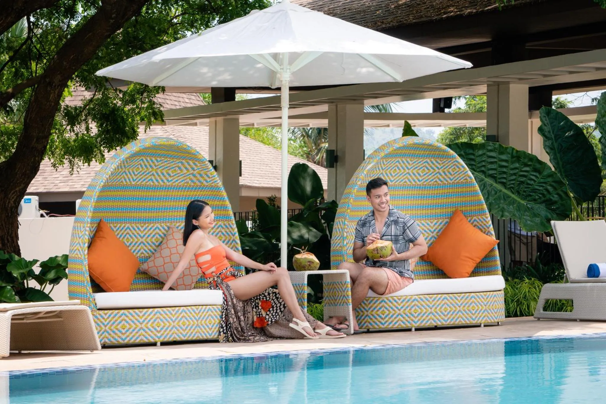 Un couple se détend dans des fauteuils colorés au bord d'une piscine.