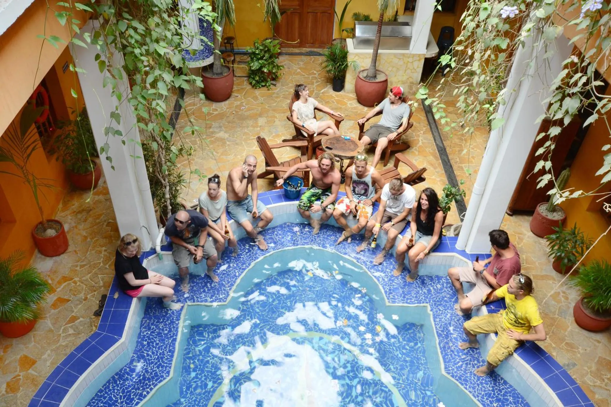 Un groupe de personnes est assis et se détend autour d'une piscine intérieure décorée de mosaïques.