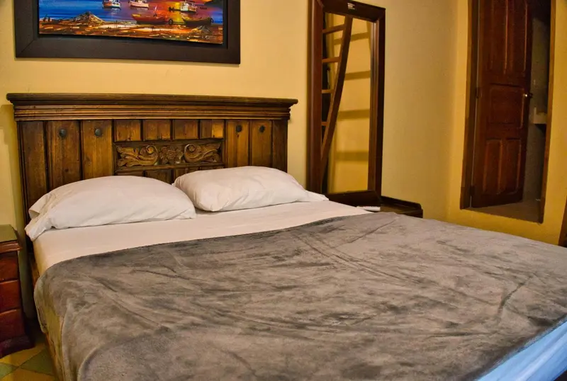 Un lit double avec une couverture grise dans une chambre aux murs jaunes.
