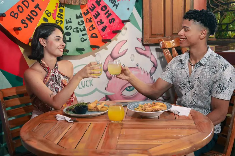 Deux personnes sourient en levant leurs verres dans un décor coloré.