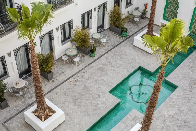 Une cour intérieure avec une piscine rectangulaire et des tables.