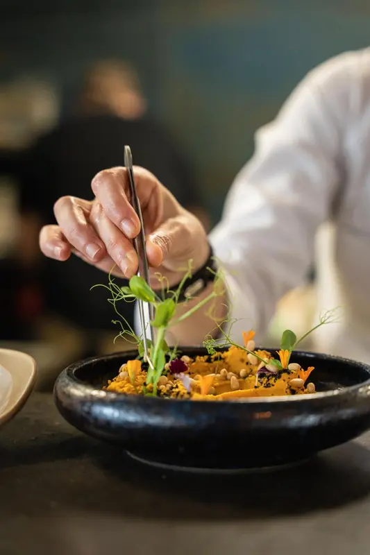 Un chef décore un plat raffiné avec une pince.