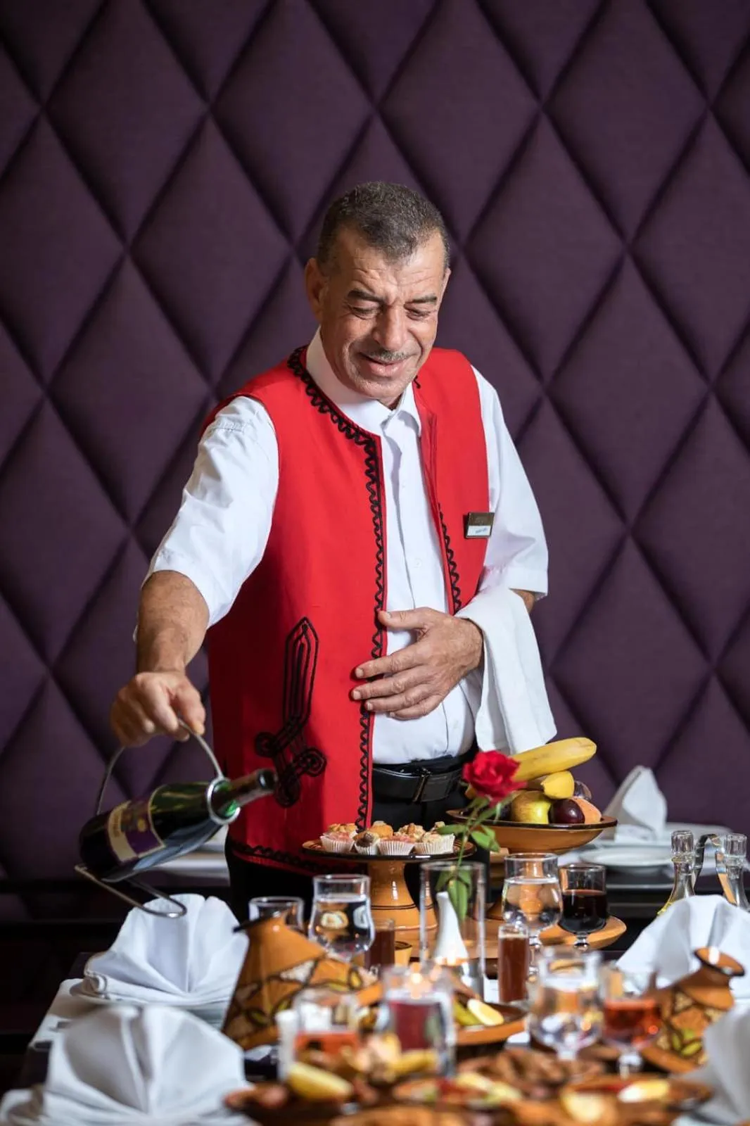 Un homme verse du vin dans un verre sur une table garnie de fruits et de nourriture.