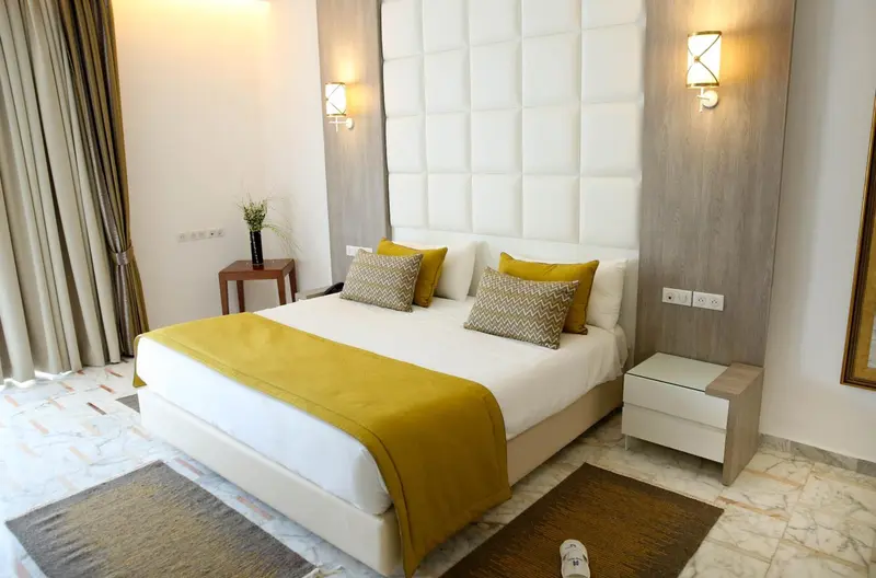 Une chambre lumineuse avec un grand lit recouvert d'une courtepointe jaune et de coussins décoratifs.
