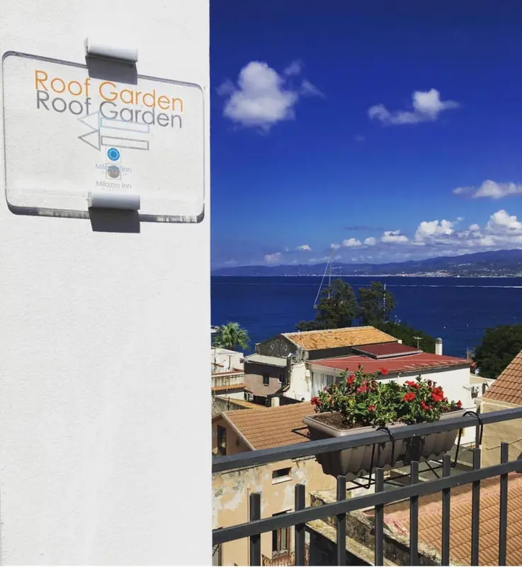 Vue panoramique sur la mer et les collines depuis une terrasse fleurie.