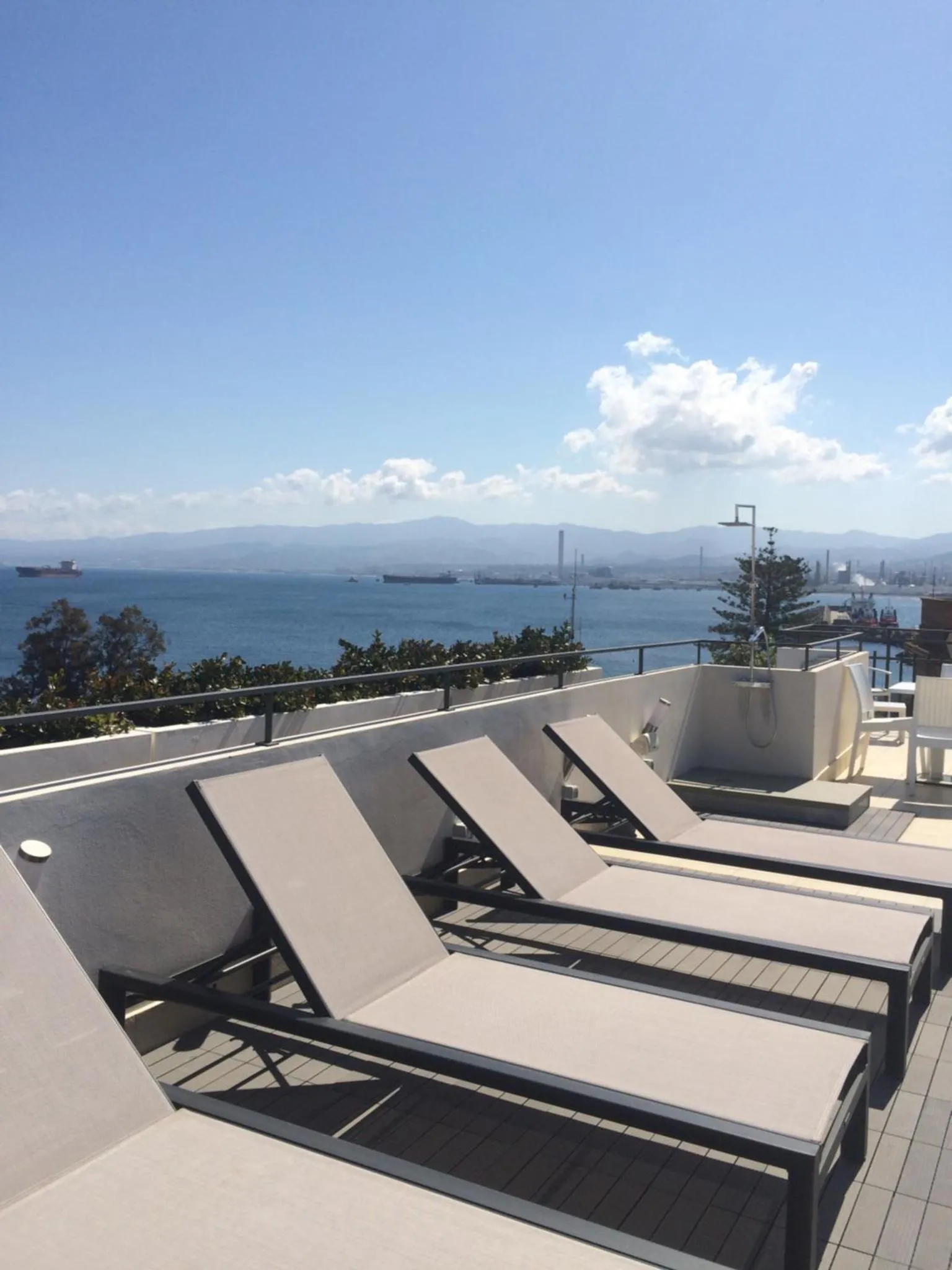 Transats alignés sur une terrasse ensoleillée avec vue sur la mer et les montagnes.