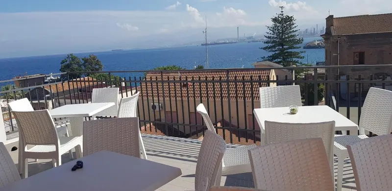Terrasse avec tables et chaises donnant sur la mer et la ville.