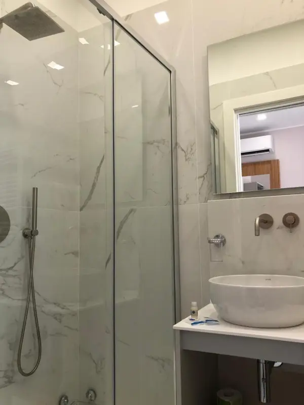 Une douche à l'italienne moderne avec des carreaux de marbre et un lavabo blanc.