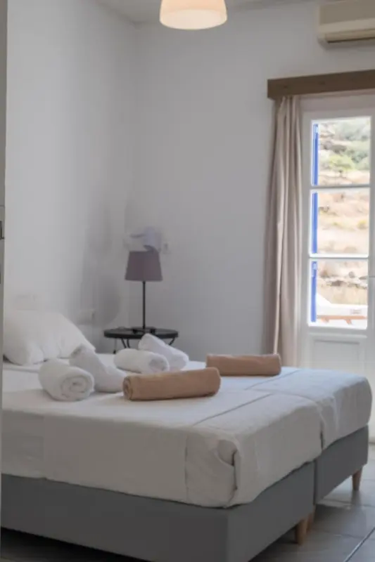 Une chambre lumineuse avec un lit préparé et une fenêtre ouverte sur un paysage.