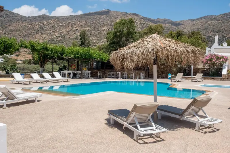 Transats et parasol à l'ombre près d'une piscine ensoleillée.