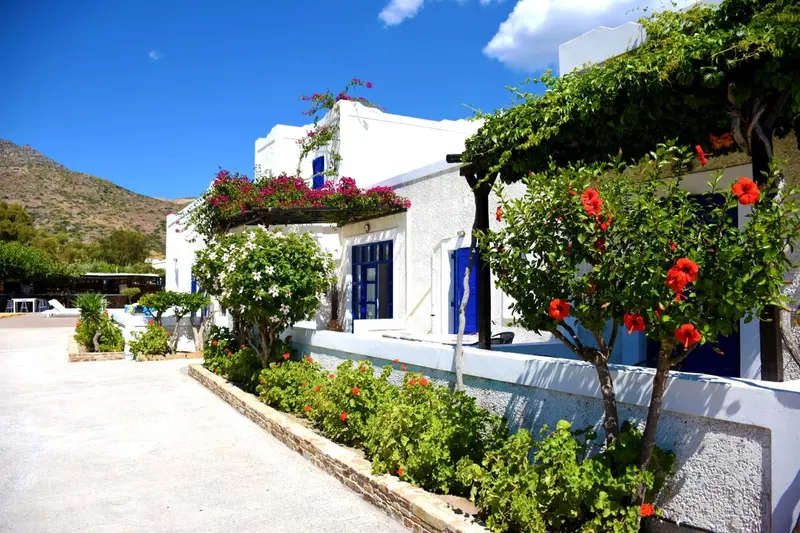 Bâtiment blanc orné de fleurs rouges et de végétation luxuriante, avec une vue sur des montagnes au loin.