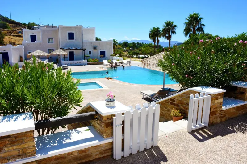 Une piscine turquoise bordée de chaises longues et de végétation luxuriante devant un bâtiment blanc.