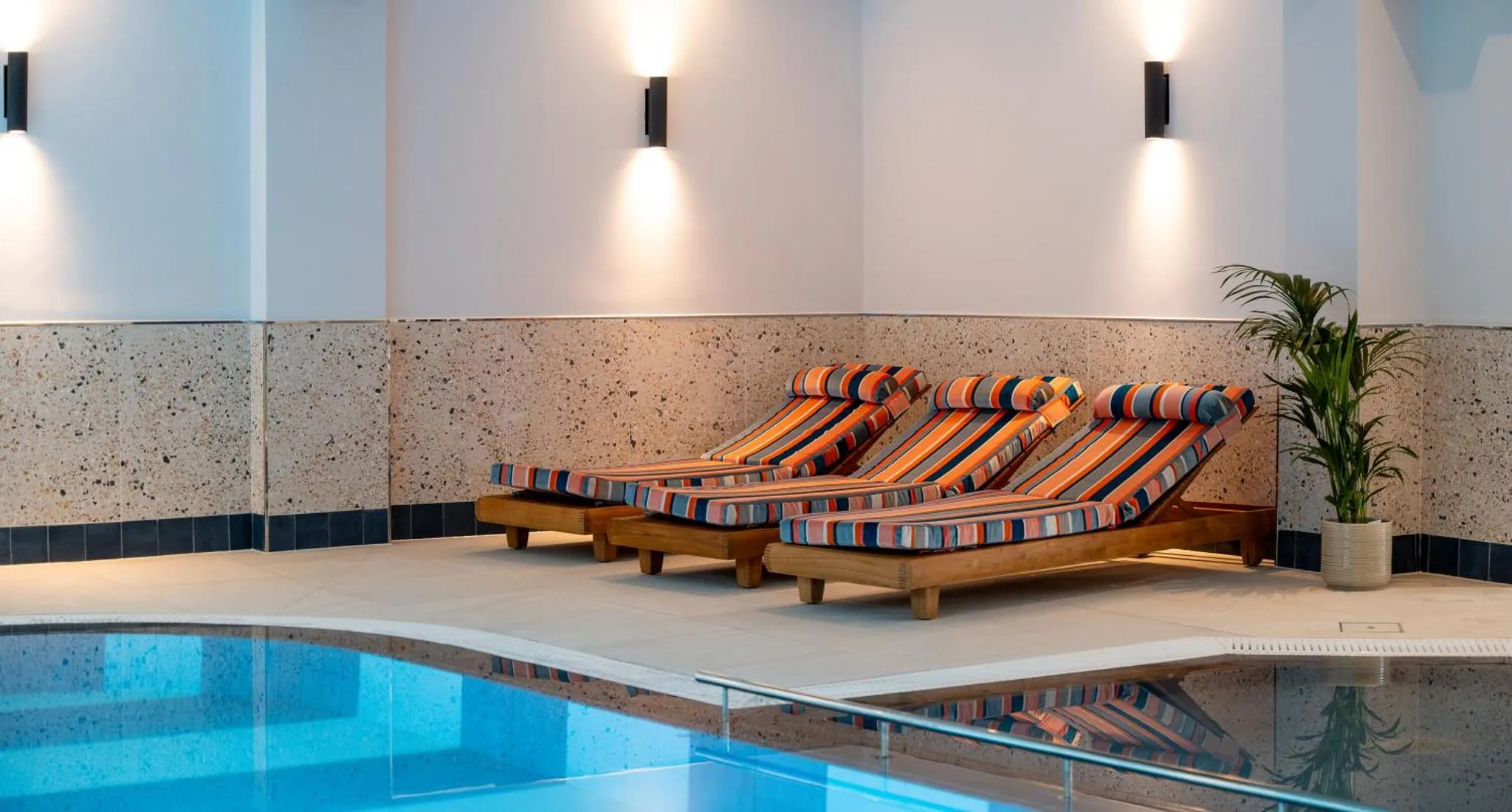 Trois transats colorés sont alignés près d'une piscine intérieure.