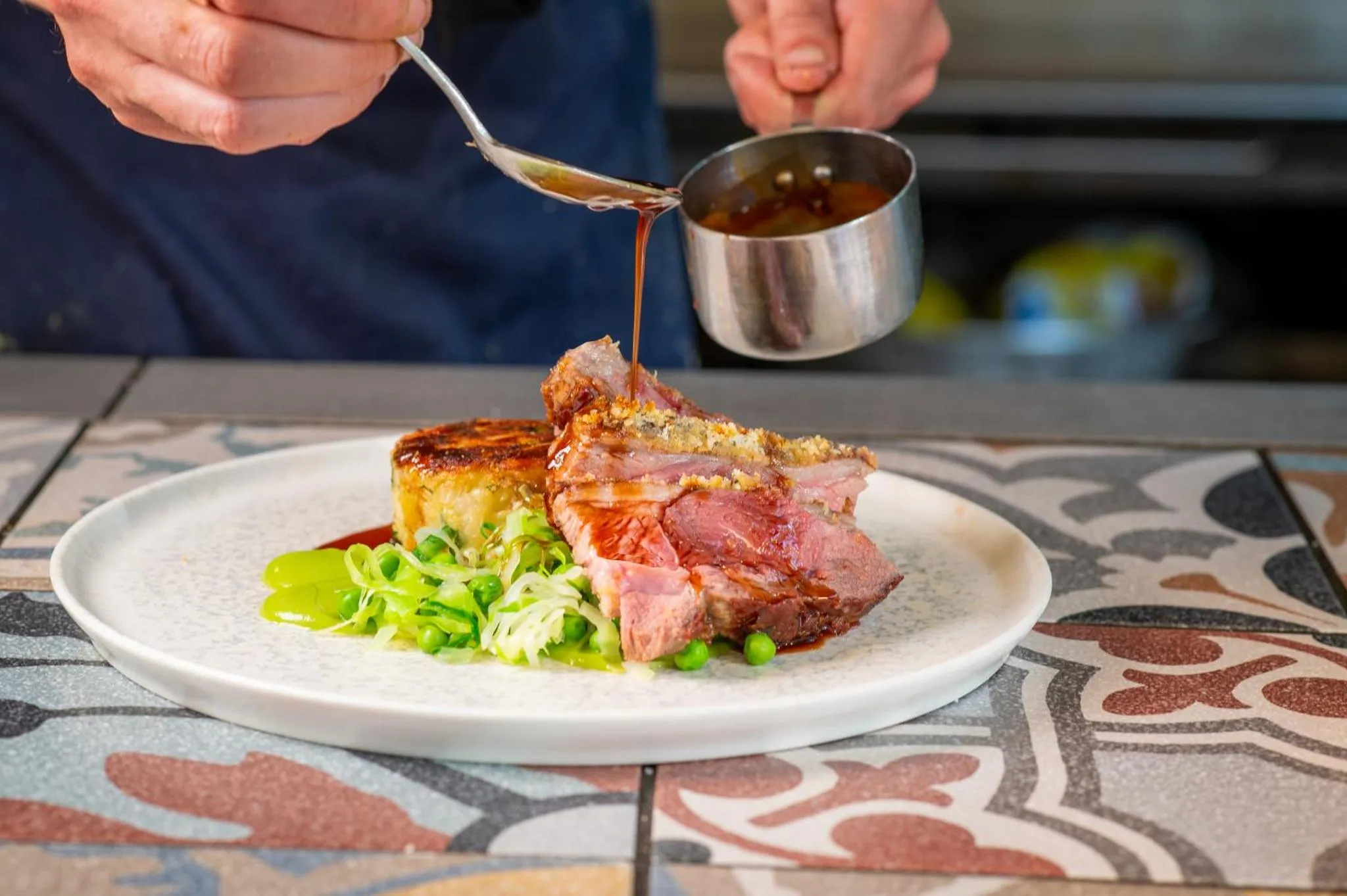 Un chef décore une assiette avec une sauce sur une portion de viande.
