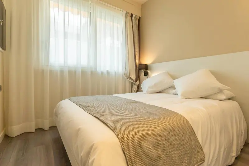 Une chambre lumineuse avec un grand lit et des rideaux clairs.