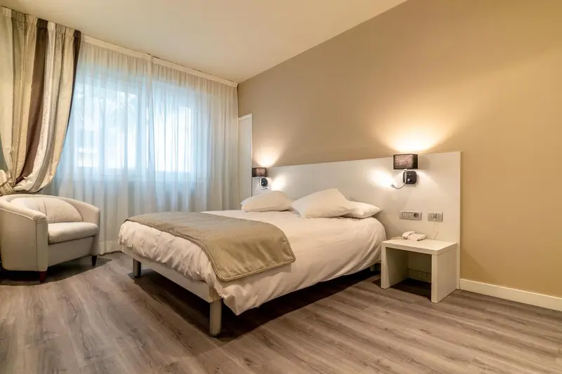 Une chambre lumineuse avec un grand lit et un fauteuil.
