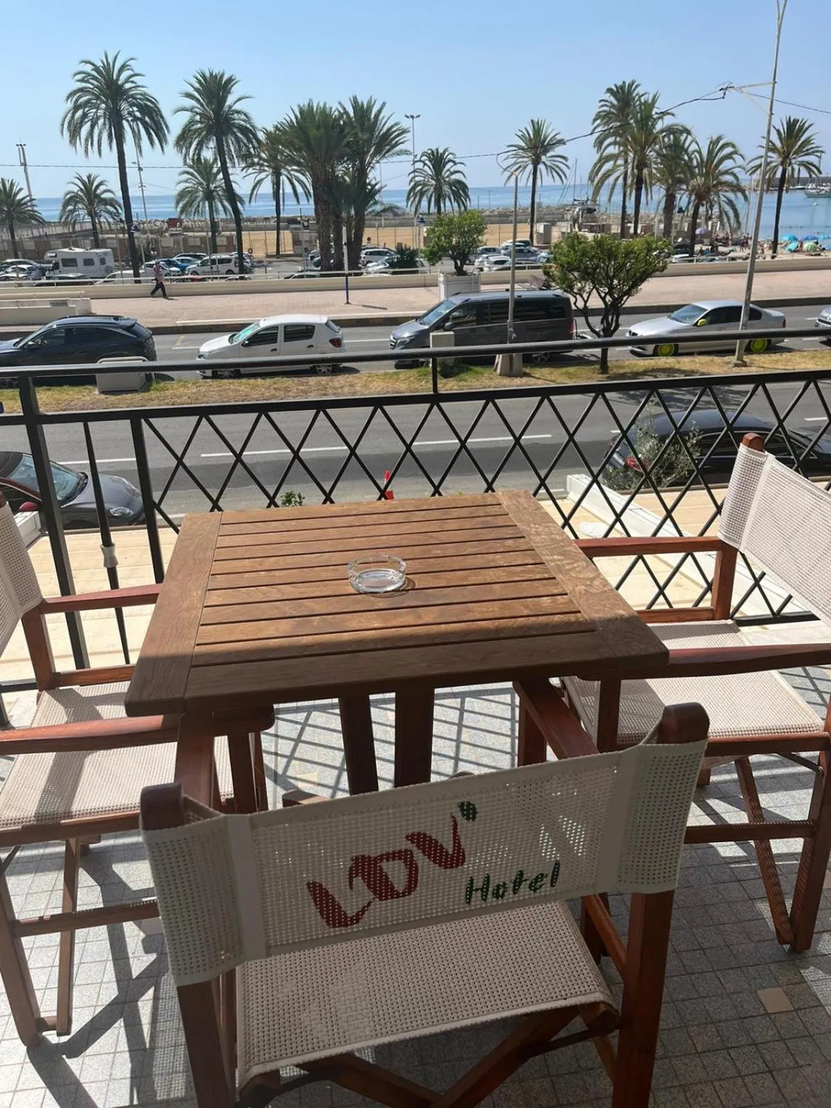 Une table et des chaises en osier sur une terrasse ensoleillée avec vue sur la mer et des palmiers.