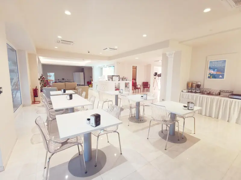 Une salle lumineuse avec des tables et des chaises blanches est prête pour le service.