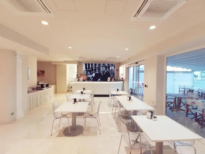 Une salle lumineuse avec des tables et des chaises blanches est prête pour le service.