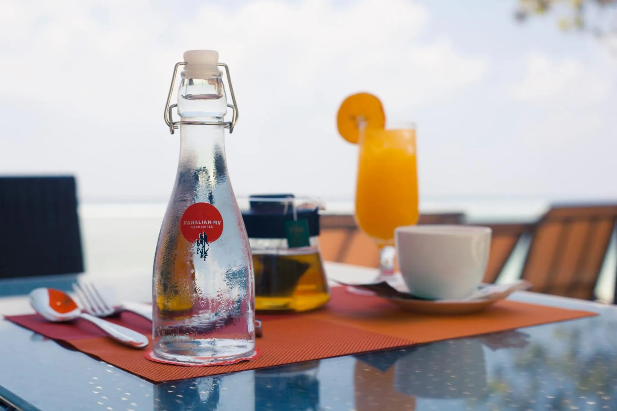Une table est dressée avec des boissons et de la vaisselle sur une terrasse.