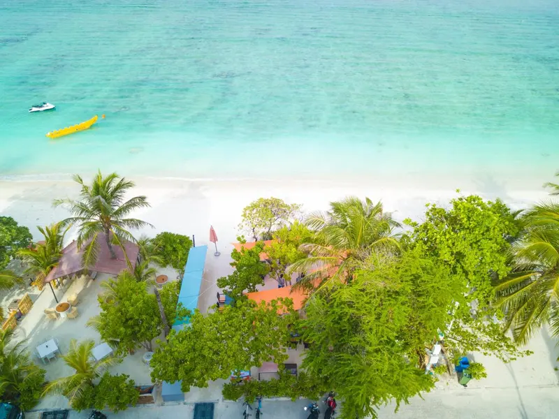 Vue aérienne d'une plage de sable blanc bordée de végétation tropicale et de quelques bungalows.