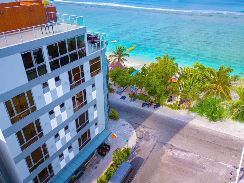 Bâtiment moderne avec balcon surplombant une plage de sable blanc et une mer turquoise.