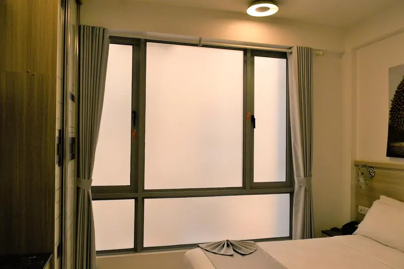 Une fenêtre lumineuse donne sur un lit soigné dans une chambre.