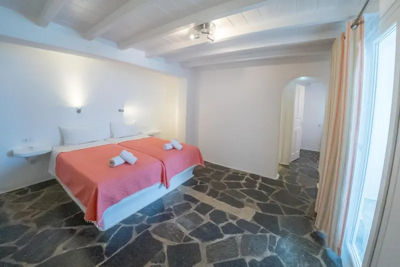 Une chambre lumineuse avec un lit double et un sol en pierre.