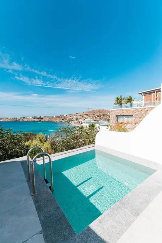 Petite piscine turquoise avec escalier en inox, vue sur la mer et le ciel bleu.
