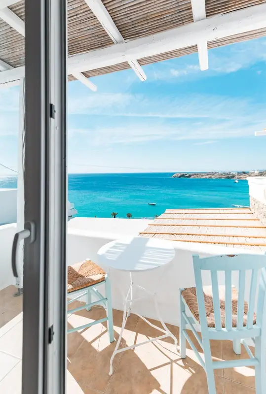 Vue sur la mer depuis une terrasse ensoleillée avec mobilier blanc et bleu.