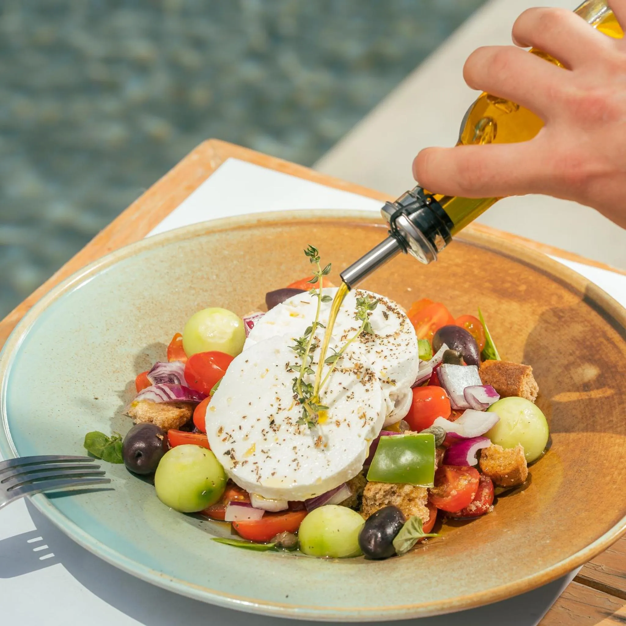 Une assiette de salade colorée est arrosée d'huile d'olive.