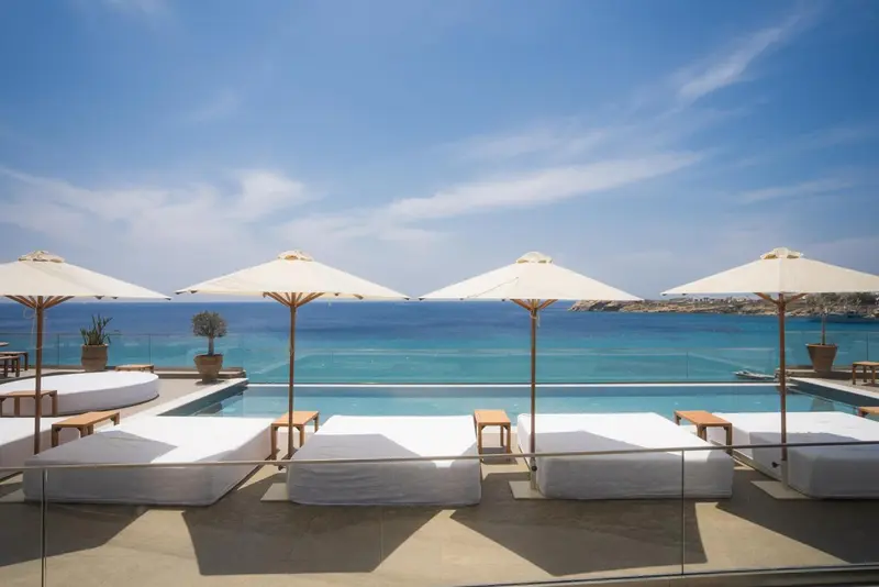 Transats blancs disposés autour d'une piscine à débordement avec vue sur la mer.