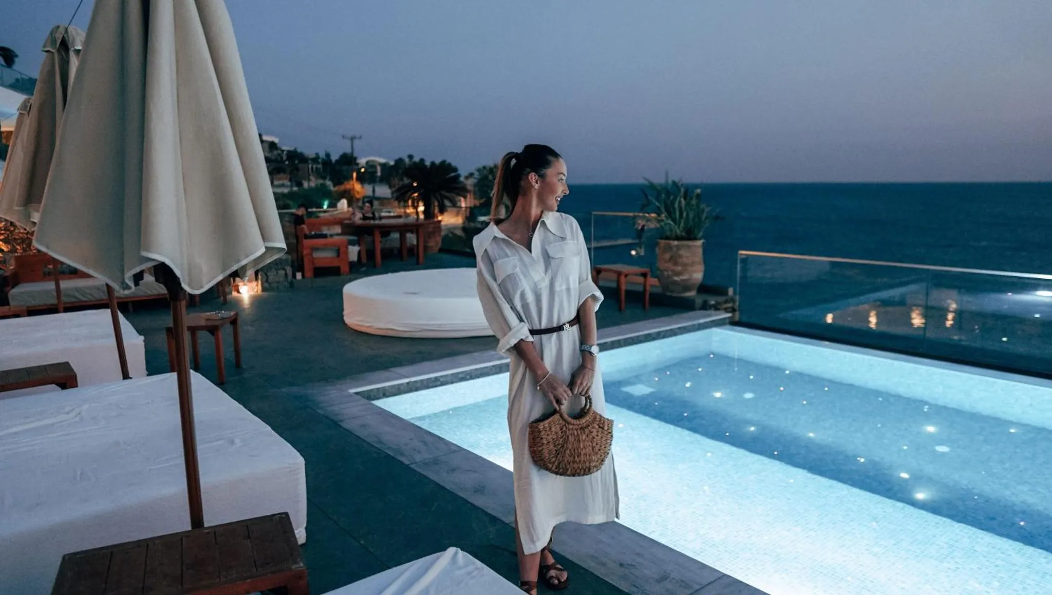 Une femme se tient près d'une piscine sur une terrasse avec vue sur la mer.