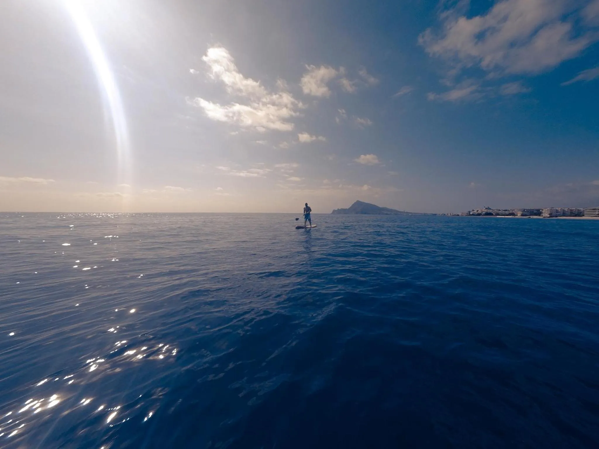 Une personne pratique le stand-up paddle sur une mer bleue sous un ciel nuageux.