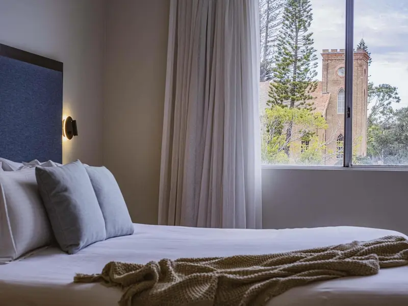 Une chambre lumineuse avec un grand lit et une vue sur un édifice religieux.