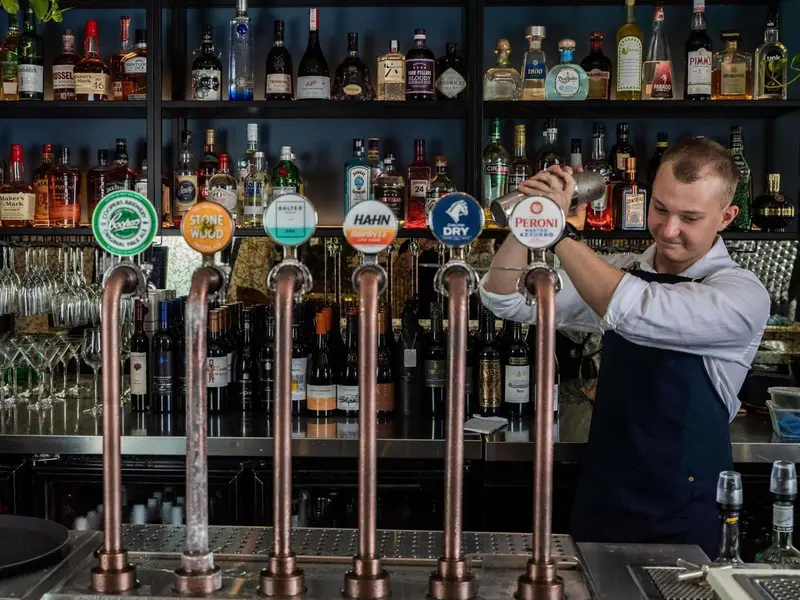 Un barman prépare une boisson derrière un comptoir bien garni de bouteilles.
