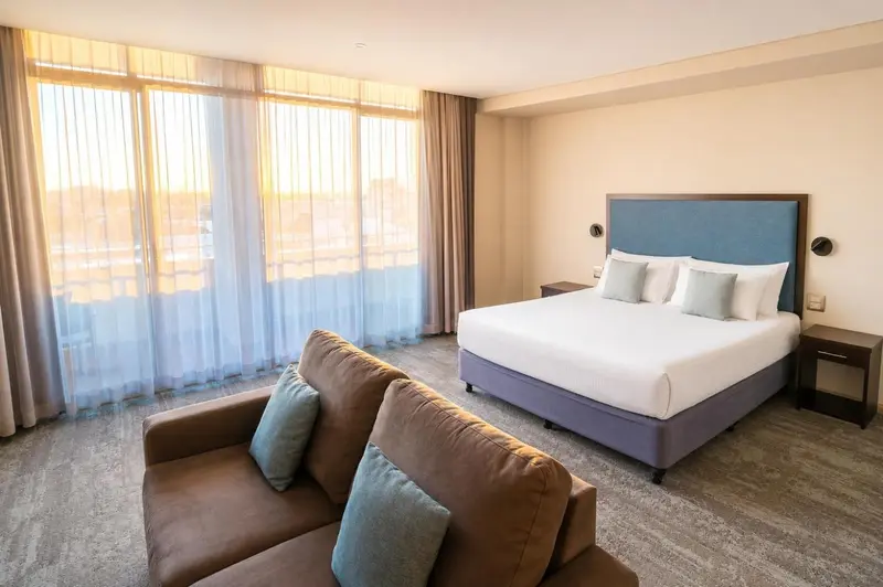 Une chambre lumineuse avec un canapé et un grand lit face à une baie vitrée.
