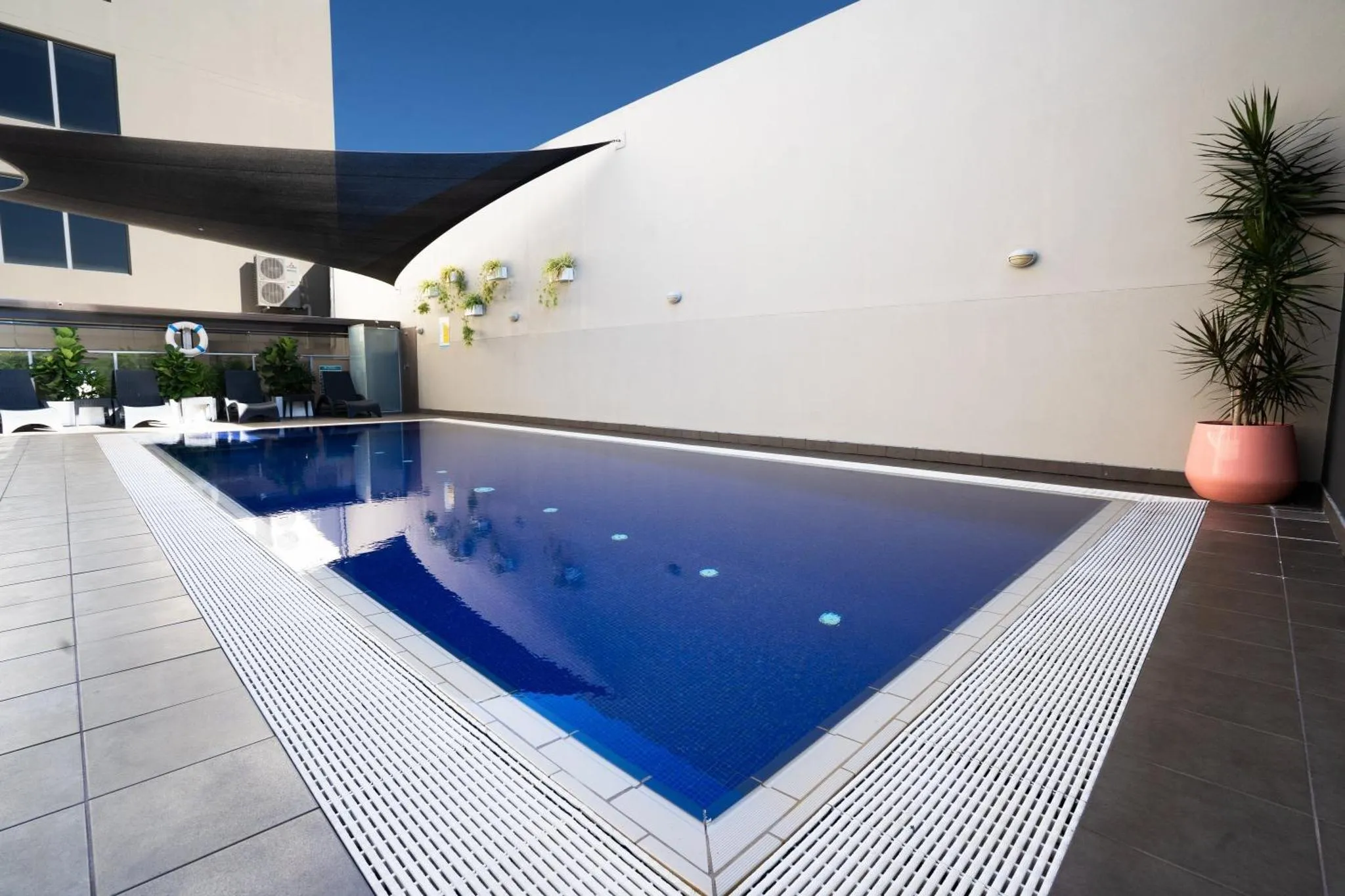 Piscine rectangulaire bleue entourée d'une terrasse carrelée.