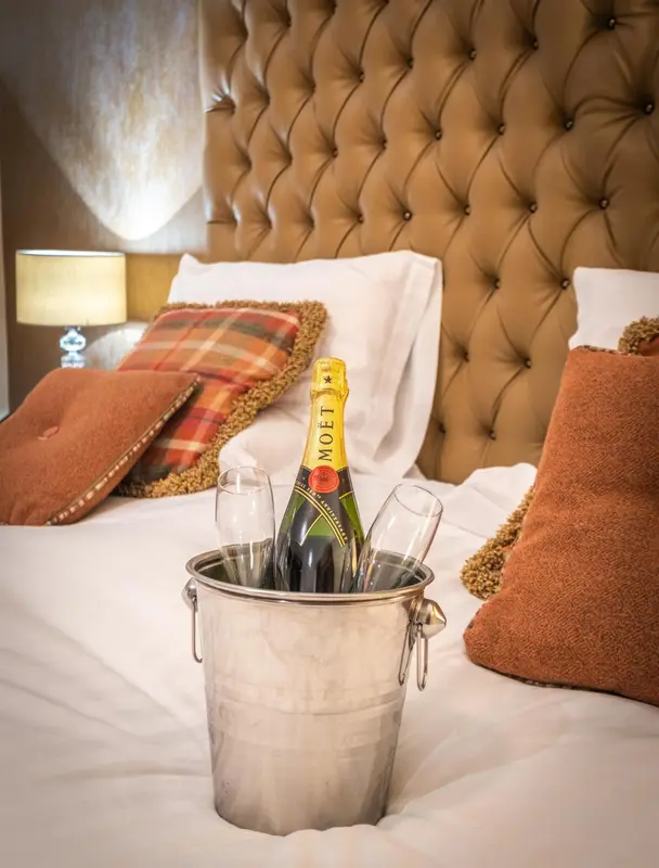 Un lit recouvert de draps blancs est orné de coussins et d'une bouteille de champagne dans un seau à glace.