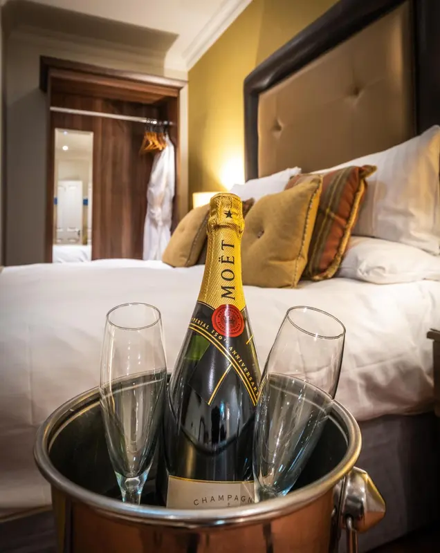 Une bouteille de champagne et deux flûtes dans un seau à glace reposent sur un lit décoré de coussins.