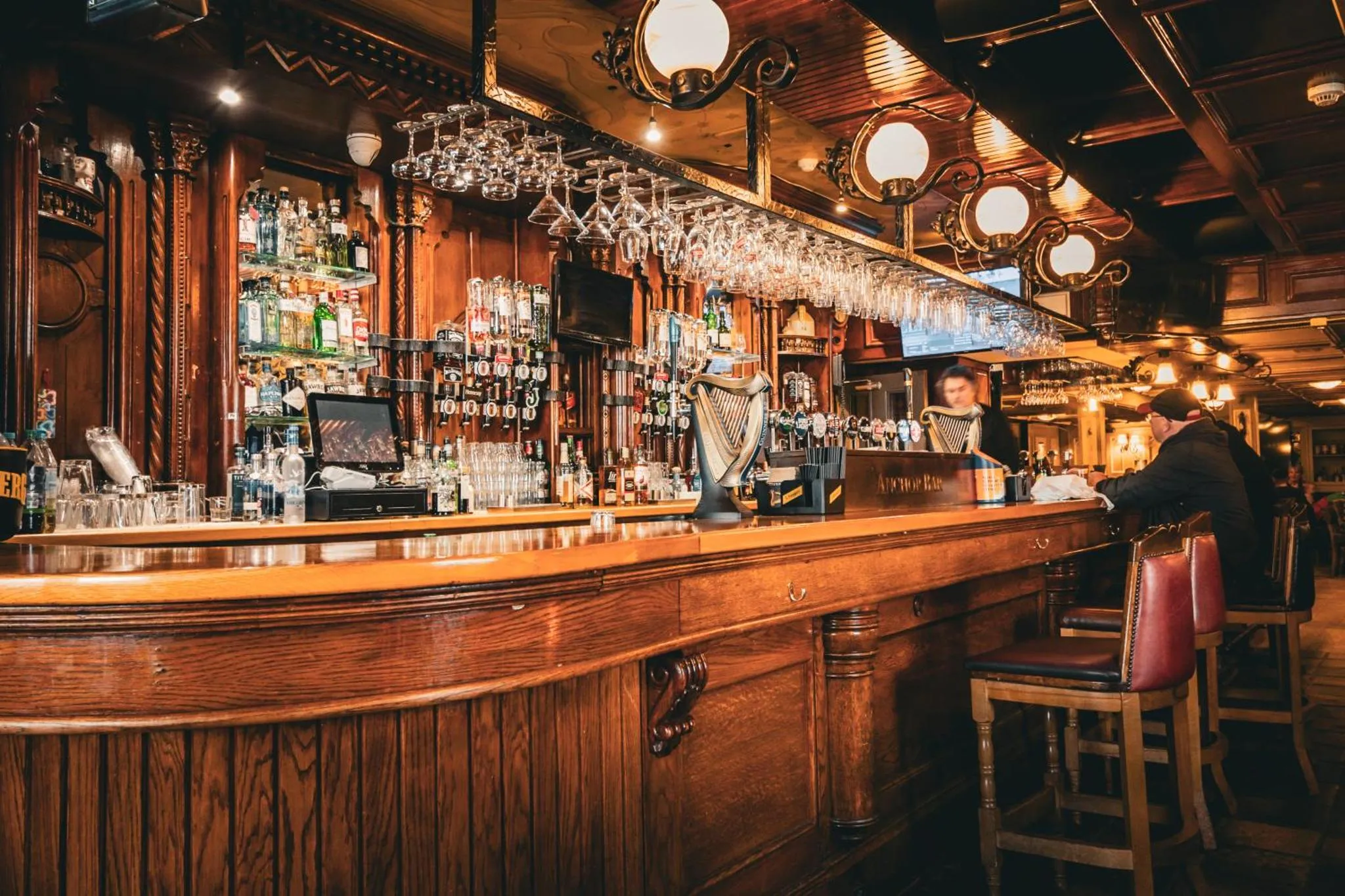 Un comptoir de bar en bois sombre est aligné de bouteilles et de verres.